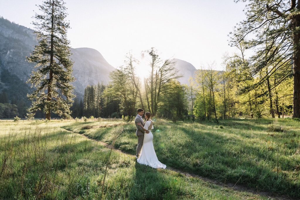 Engaged couple walking beneath tall pines in Yosemite Valley, golden sunrise light filtering through trees